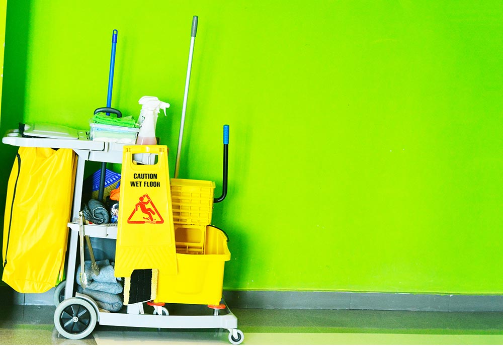 A cleaning cart sits parked against a lime green wall.